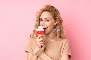Young blonde woman holding a cornet ice cream isolated on pink background