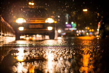 Rainy night in the big city, approaching headlights of car traveling along the avenue. View from the level of the curb on the road