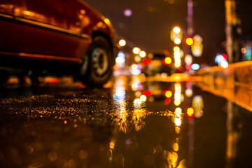 Rainy night in the big city, car passing nearby. View from the level of the puddles near the border