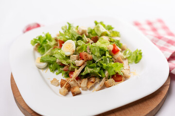 Caesar salad with chicken and eggs on a white plate close up