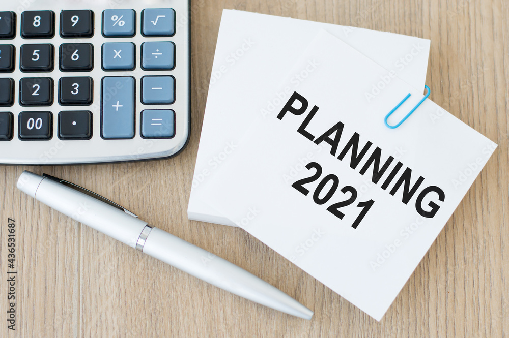 Poster a card with a text of planning 2021 on a wooden table next to a pen and a calculator