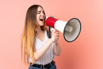 Young caucasian woman isolated on pink background shouting through a megaphone