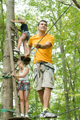 Naklejka na ściany i meble adult male walking across rope bridge between the trees