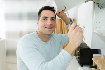 man posing while fixing cupboard hinges