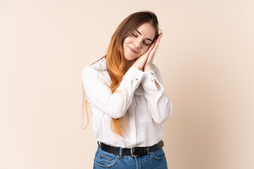 Young caucasian woman isolated on beige background making sleep gesture in dorable expression