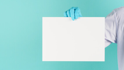 Blank board paper in doctor hand.Man wear blue latex glove and doctor on mint green or Tiffany Blue background.