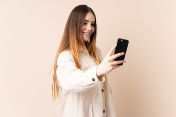 Fototapeta premium Young caucasian woman isolated on beige background making a selfie