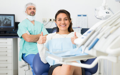 Obraz premium Portrait of smiling satisfied american woman visiting dentist giving thumbs up