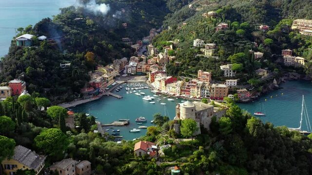 Aerial view of the harbor of Portofino in italy with boats sailing in the water. We can see the city in the middle of forest and mountain near the water 4K