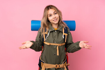 Teenager Russian mountaineer girl with a big backpack isolated on pink background smiling
