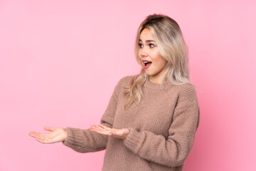 Teenager blonde girl wearing a sweater over isolated pink background with surprise facial expression