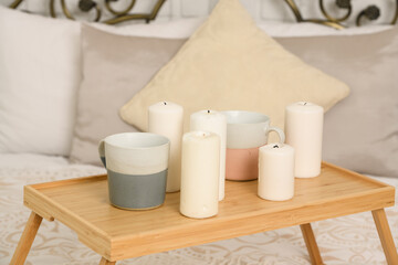 A close-up of a stand with two cups and candles stands on a light bed. the concept of breakfast in bed, home comfort, romance.