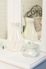 A glamorous dressing table. A table for the lady. White fashion box, space for text. On the table is a white vase and a glass jar. You can see the mirror. Vertical frame