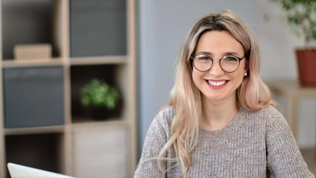 Portrait of adorable blonde female in glasses laughing with healthy dental smile posing at workplace