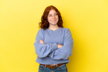 Teenager reddish woman isolated on yellow background making doubts gesture while lifting the...