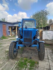 old blue tractor Belarus stands in the courtyard of a country house