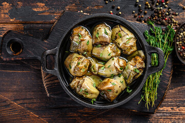 Marinated artichokes in olive oil in a pan. Dark wooden background. Top view
