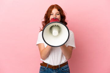 Teenager reddish woman isolated on pink background shouting through a megaphone to announce...
