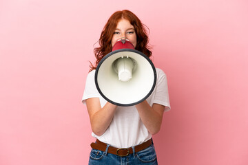 Teenager reddish woman isolated on pink background shouting through a megaphone to announce something