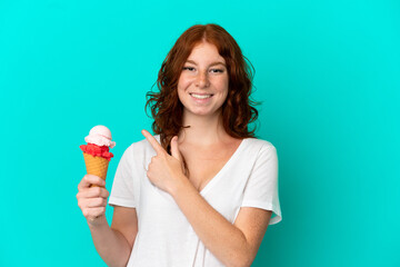 Teenager reddish woman with a cornet ice cream isolated on blue background pointing to the side to present a product