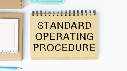 Standard Operating Procedure text on paper in open diary with spectacles, colourful push pin, pen and calculator on the wooden table - business and finance concept