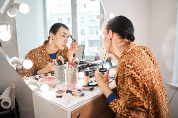 Drag queen sitting in front of the mirror and puts on makeup