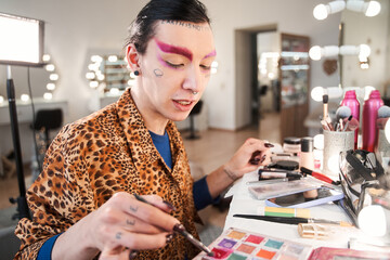 Drag queen with pink brows choosing colors for his makeup