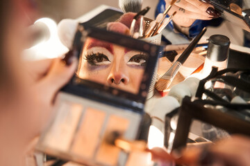 Reflexion at the hand mirror of the face of drag queen making bright makeup - obrazy, fototapety, plakaty