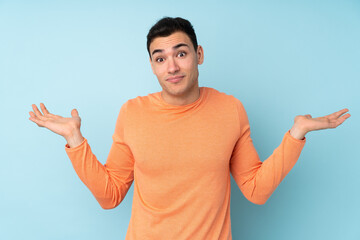 Young caucasian handsome man isolated on blue background making doubts gesture