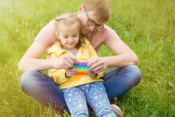 dad and daughter together in the park, holding a toy pop it
