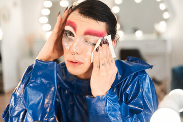 Drag queen remove his vivid makeup while sitting in front of the mirror
