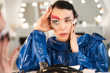 Drag queen remove his vivid makeup while sitting in front of the mirror