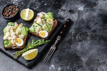 Fresh toasts with shrimp, prawns, quail eggs and cucumber on rye bread. Black background. top view. Copy space
