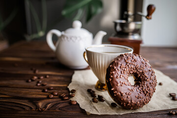 Chocolate doughnut for morning breakfast. White vintage Coffee Cup With Beans On Rustic Table