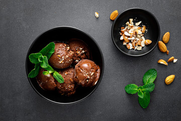 Chocolate ice cream with almonds served in bowl on black background, top view