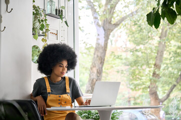 Young happy African American college student hipster girl with afro hair sitting at table in cafe...