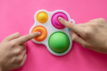 colorful trendy antistress sensory toy fidget push pop it and simple dimple in kid's hands, children share toys and playing together on pink background