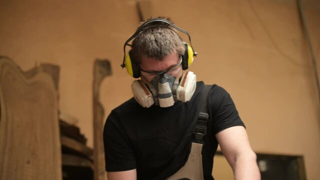 Close-up of a carpenter working in a workshop using safety goggles, noise ear muffs and a respirator
