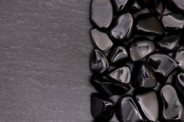 Obsidian heap jewel stones texture on half black stone background. Place for text.