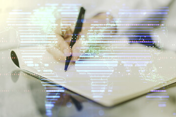 Double exposure of abstract digital world map and man hand writing in notebook on background, research and strategy concept