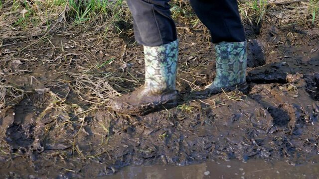 Close-up of female feet walking in the mud in rubber boots.