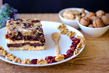 Piece of tasty chocolate-nut cake on a white plate. Walnuts and wooden spoon stand nearby