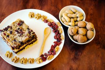 Piece of tasty chocolate-nut cake on a white plate. Walnuts and wooden spoon stand nearby