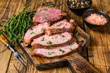 Rare slices of Roast beef sirloin tri tip steak bbq on a wooden cutting board. wooden background. Top view