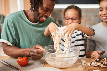 Father helping to his daughter adding and mixing ingredients in dough