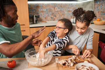 Father feeling playful with his multiracial daughters, while preparing homemade vegetarian pizza