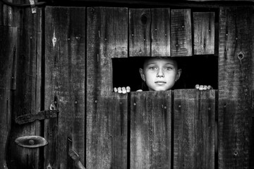 A little girl out peeks anxiously through a crack in the closed door. Black and white photo.