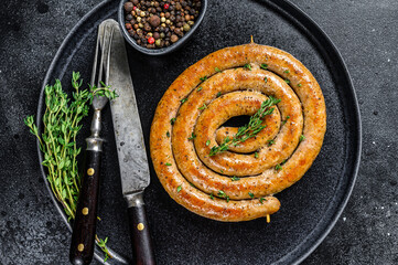 Roasted spicy spiral meat sausage on a plate. Black background. Top view