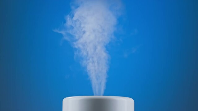 White humidifier at blue background. Ultrasonic humidifier atomizes water vapor. Humidification. Health care concept. 4k, UHD