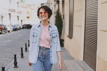 Young smiling happy student pedestrian caucasian woman 20s wearing casual jeans clothes eyeglasses strolling walk go down city street outdoors look camera People youth active urban lifestyle concept